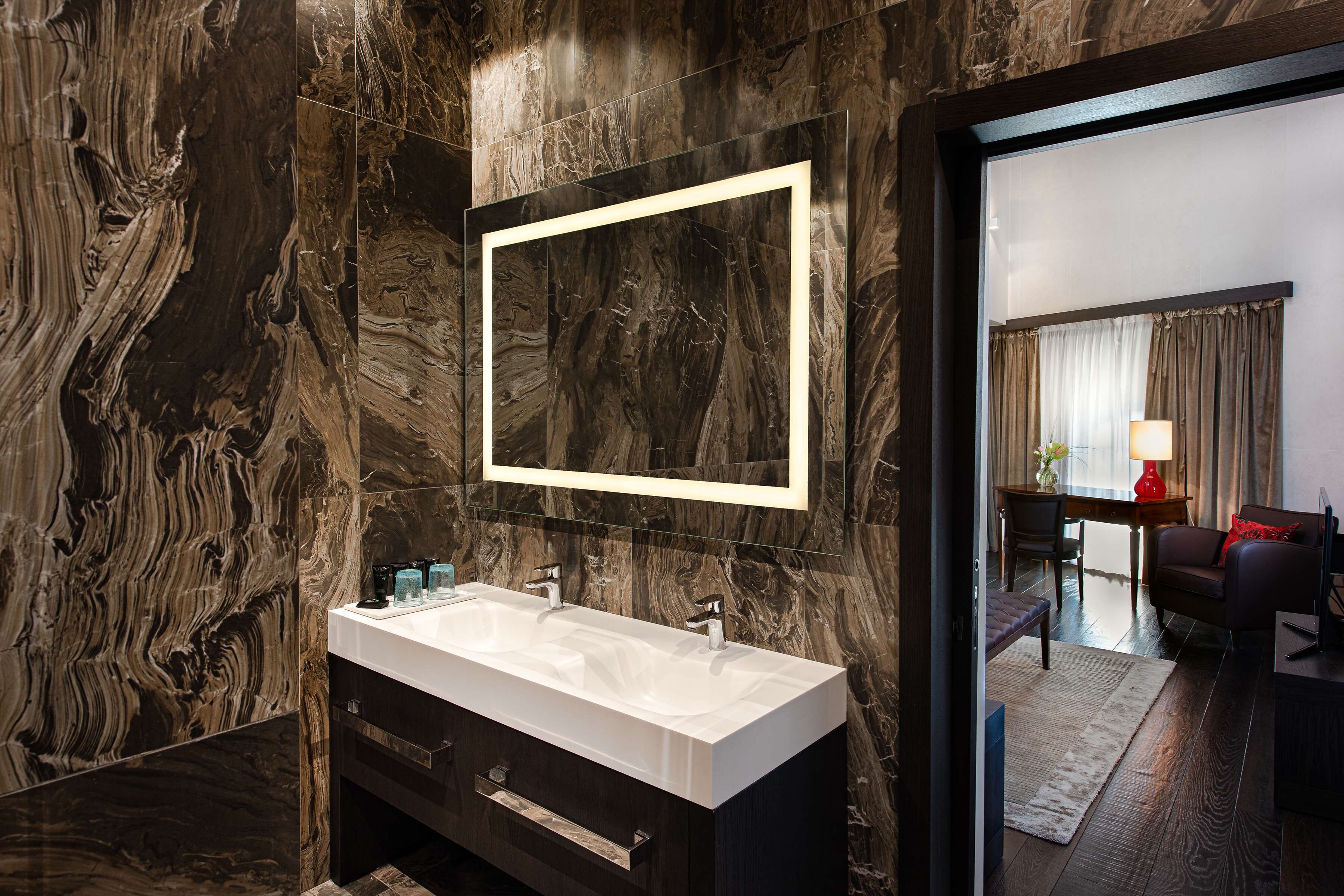 A modern bathroom with a large marble sink, dark cabinetry, and a large mirror.