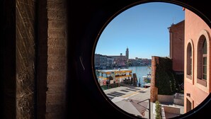 Vista a través de un ventanal circular de una zona ribereña con edificios, un barco y una torre.