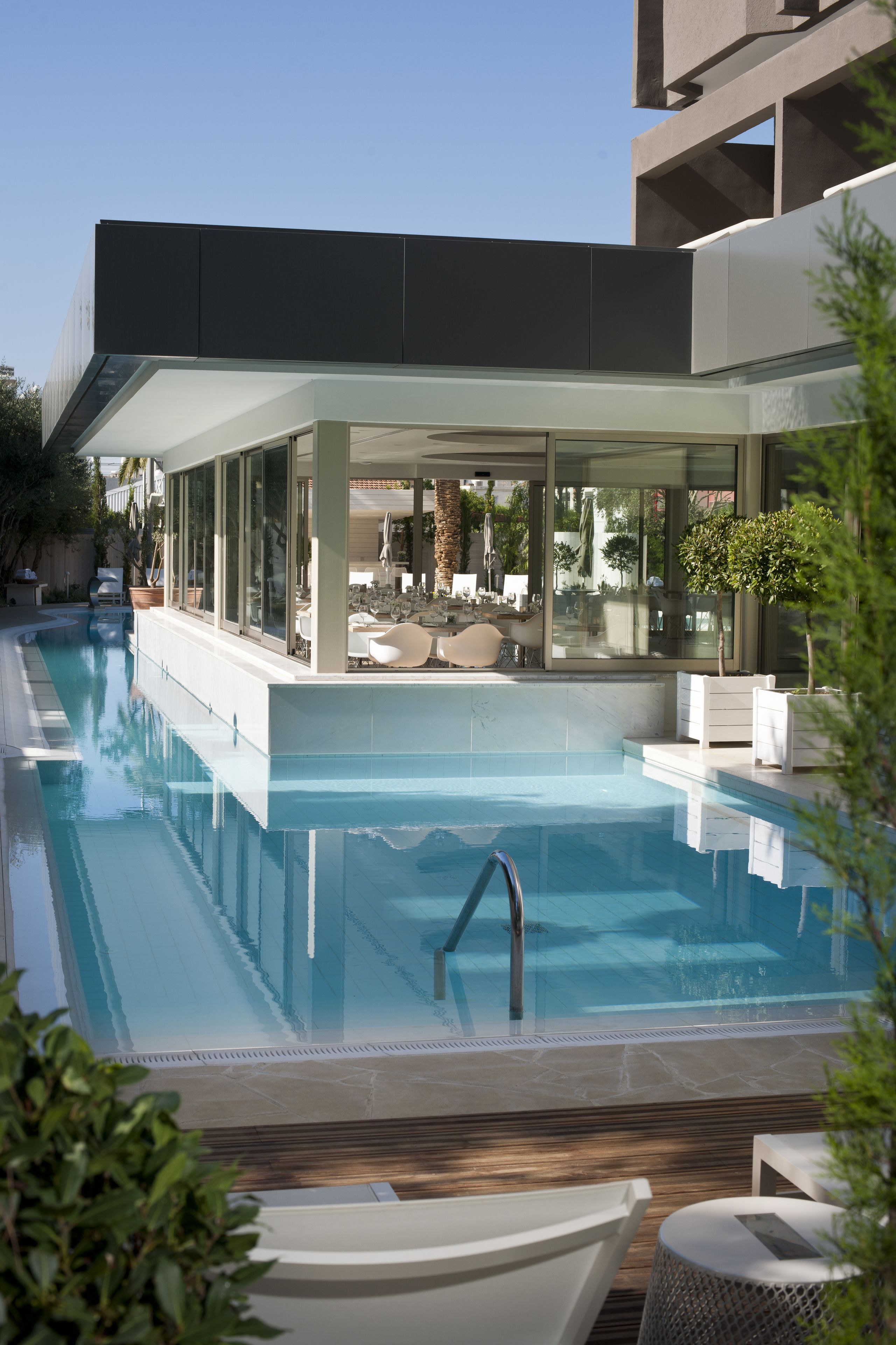 Ein moderner Poolbereich mit klarem, blauem Wasser, einer Sonnenterrasse mit Sitzgelegenheiten und Blick auf die umliegenden Gebäude.