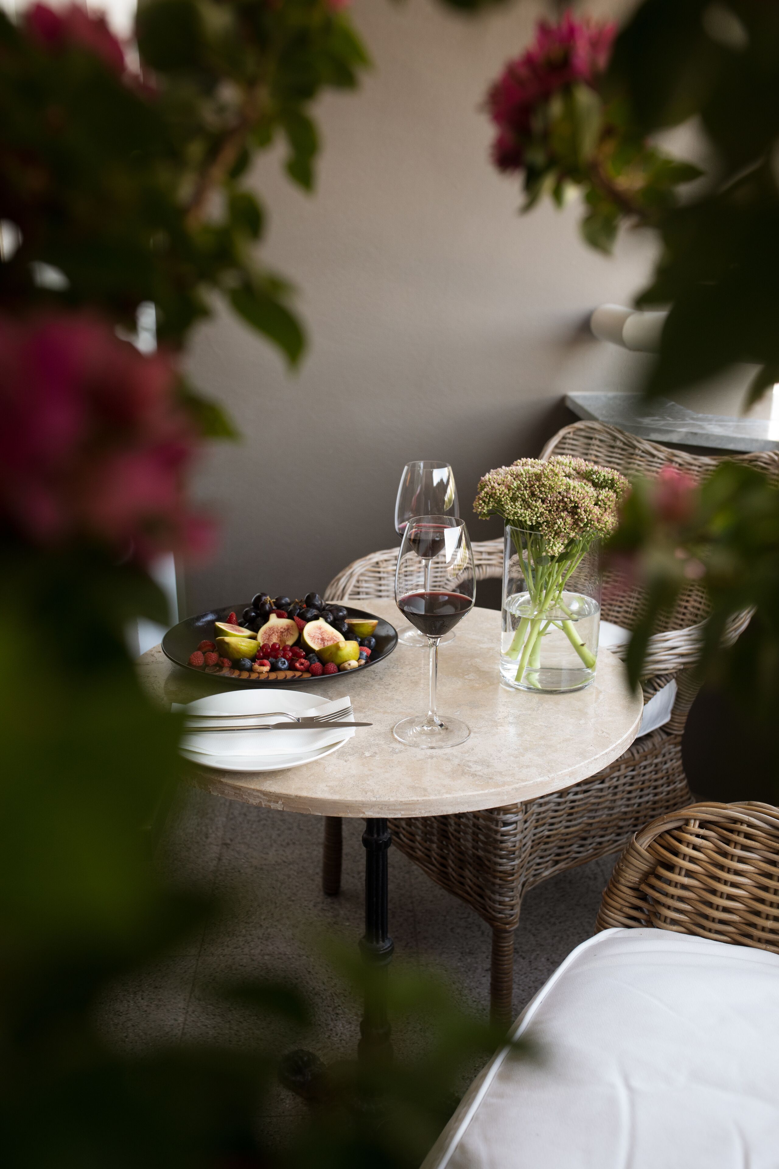 Une table ronde sur laquelle se trouvent une assiette de fruits, deux verres à vin et un vase de fleurs.
