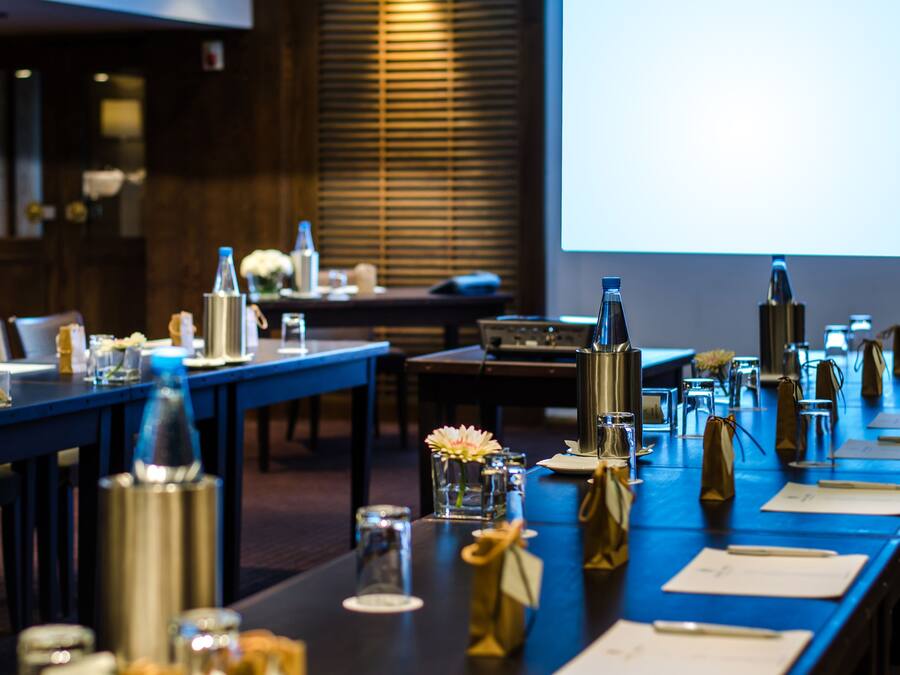 A conference room with a long table set for a meeting, equipped with microphones, nameplates, and various beverages.