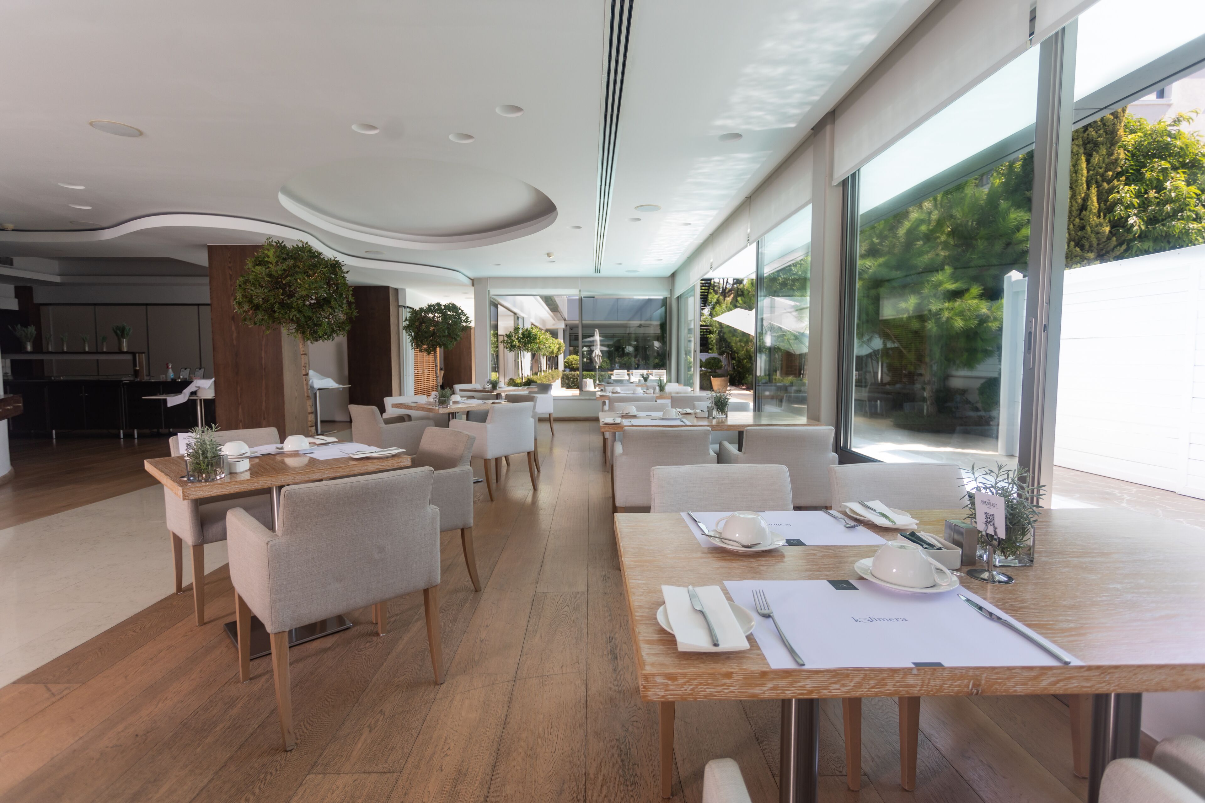 Un comedor moderno con mesas de madera, sillas blancas y plantas en macetas.