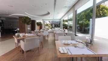 Un comedor moderno con mesas de madera, sillas blancas y plantas en macetas.