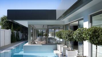 Una casa moderna con piscina, mobiliario exterior y plantas en macetas.