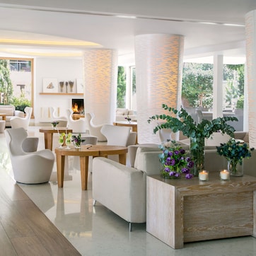 A modern interior with a wooden floor, white furniture, and large windows offering a view of greenery.