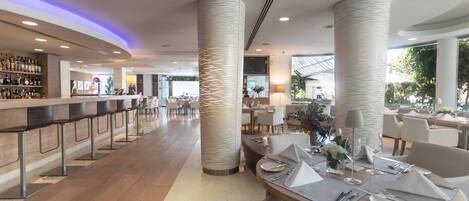 A modern restaurant with a bar area, high ceilings, and large windows.