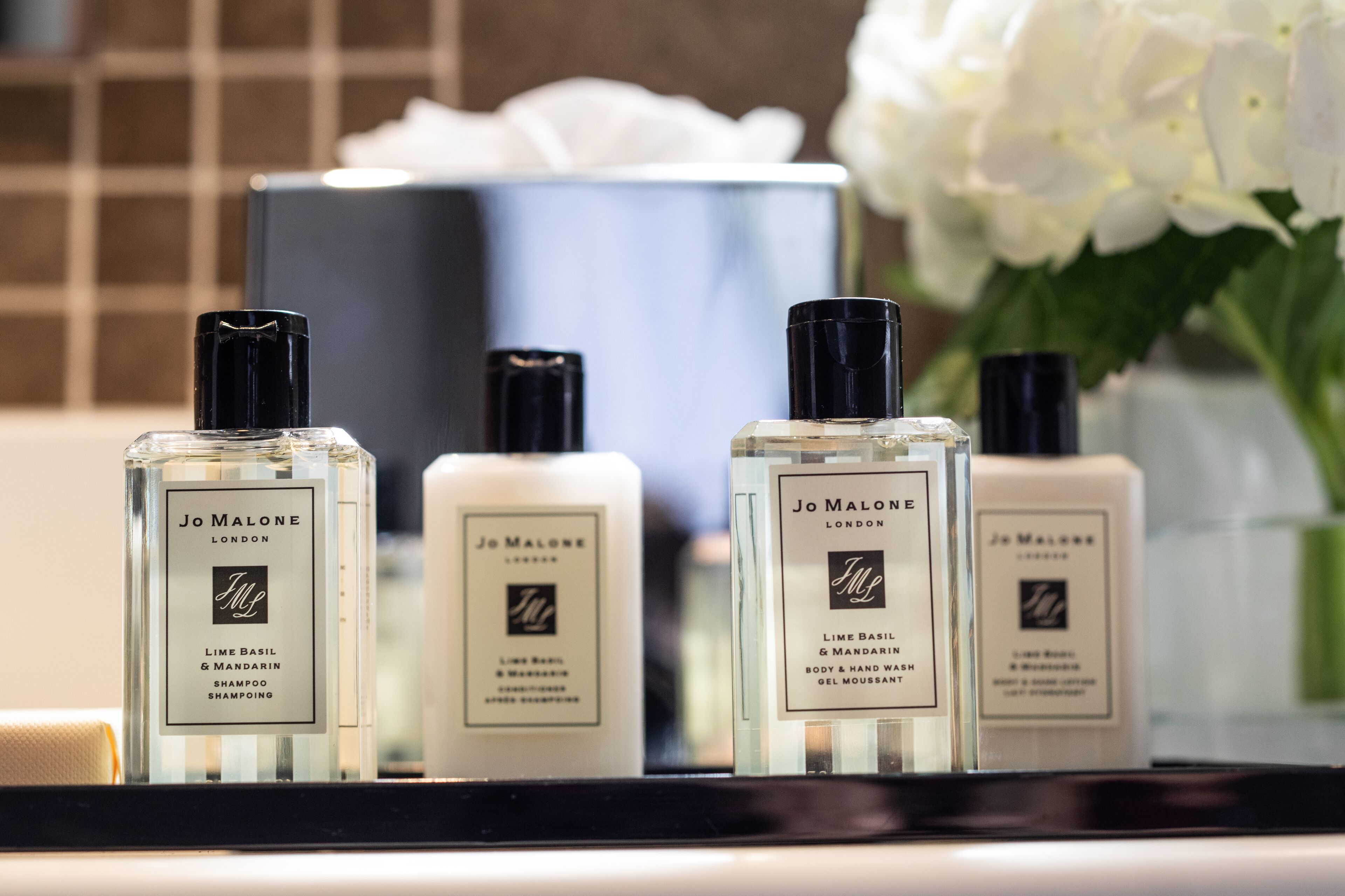 Four bottles of Jo Malone London shampoo and body wash on a reflective surface.