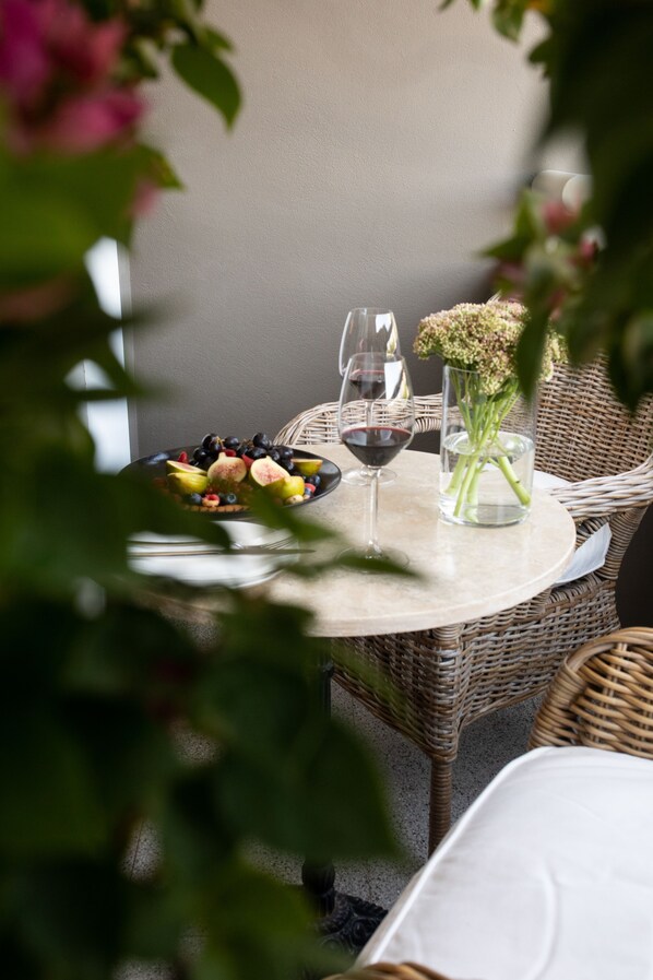 A round table with a plate of fruit, two wine glasses, and a vase with flowers.