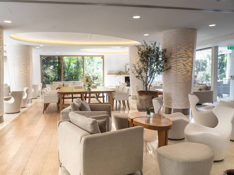 Un moderno vestíbulo de hotel con una zona de estar central, ventanas amplias y suelo de madera.
