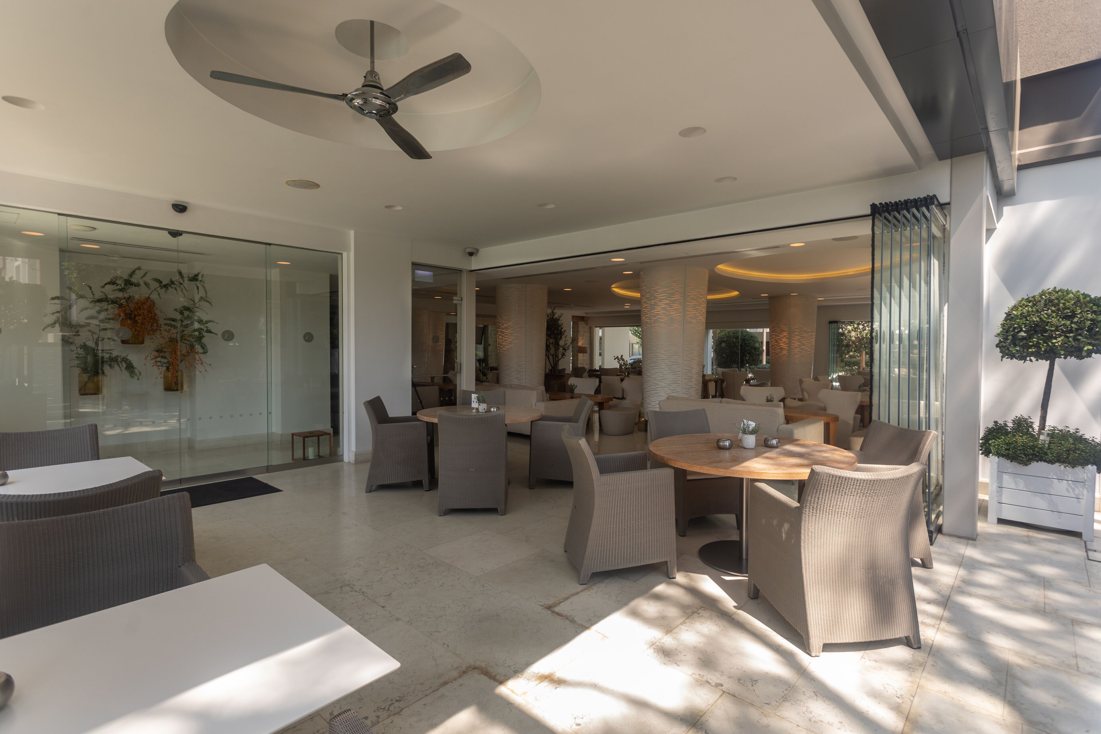A modern indoor patio area with wicker furniture, a ceiling fan, and glass walls.