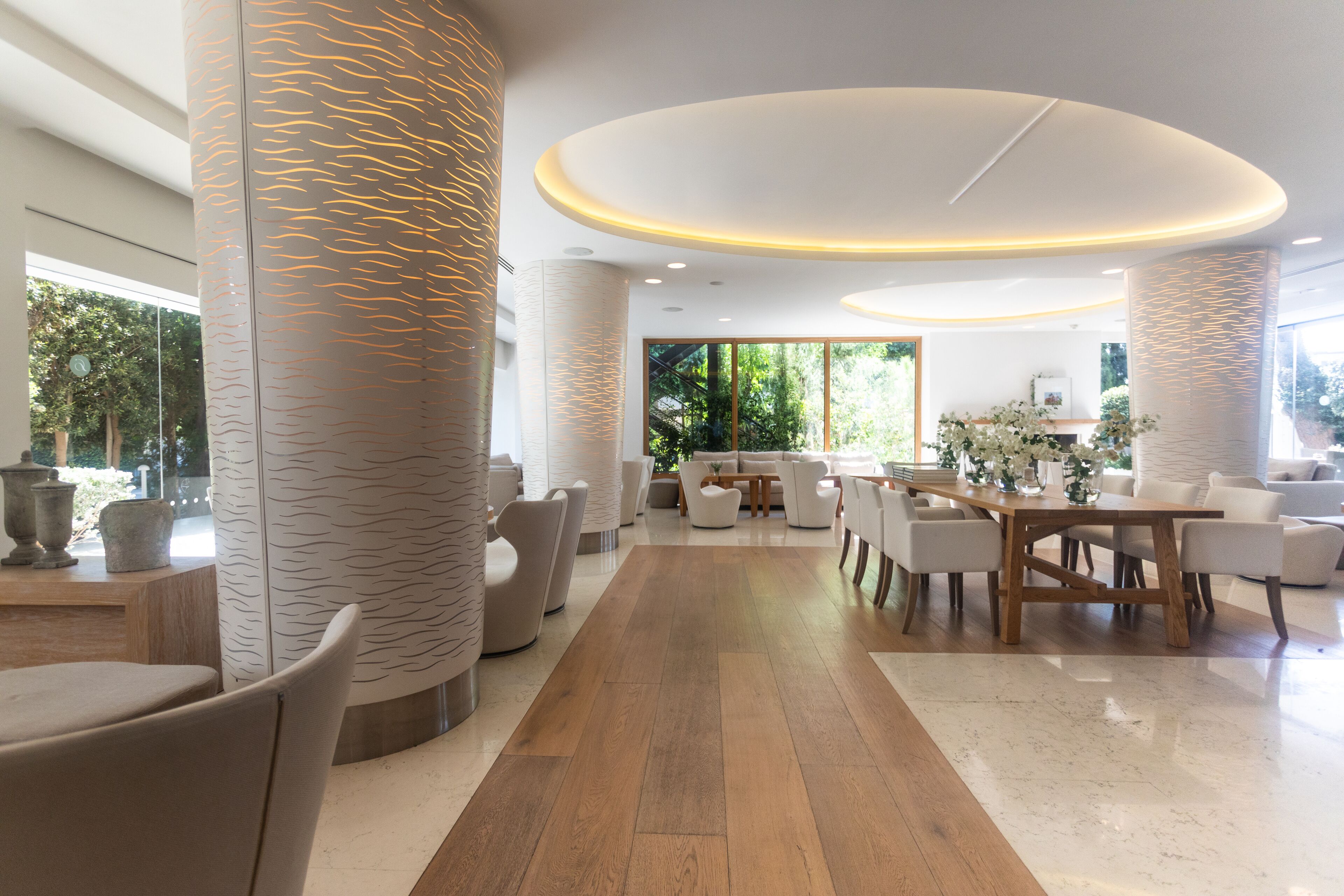 A spacious, modern interior with a central dining area, large columns, and a view of greenery outside.