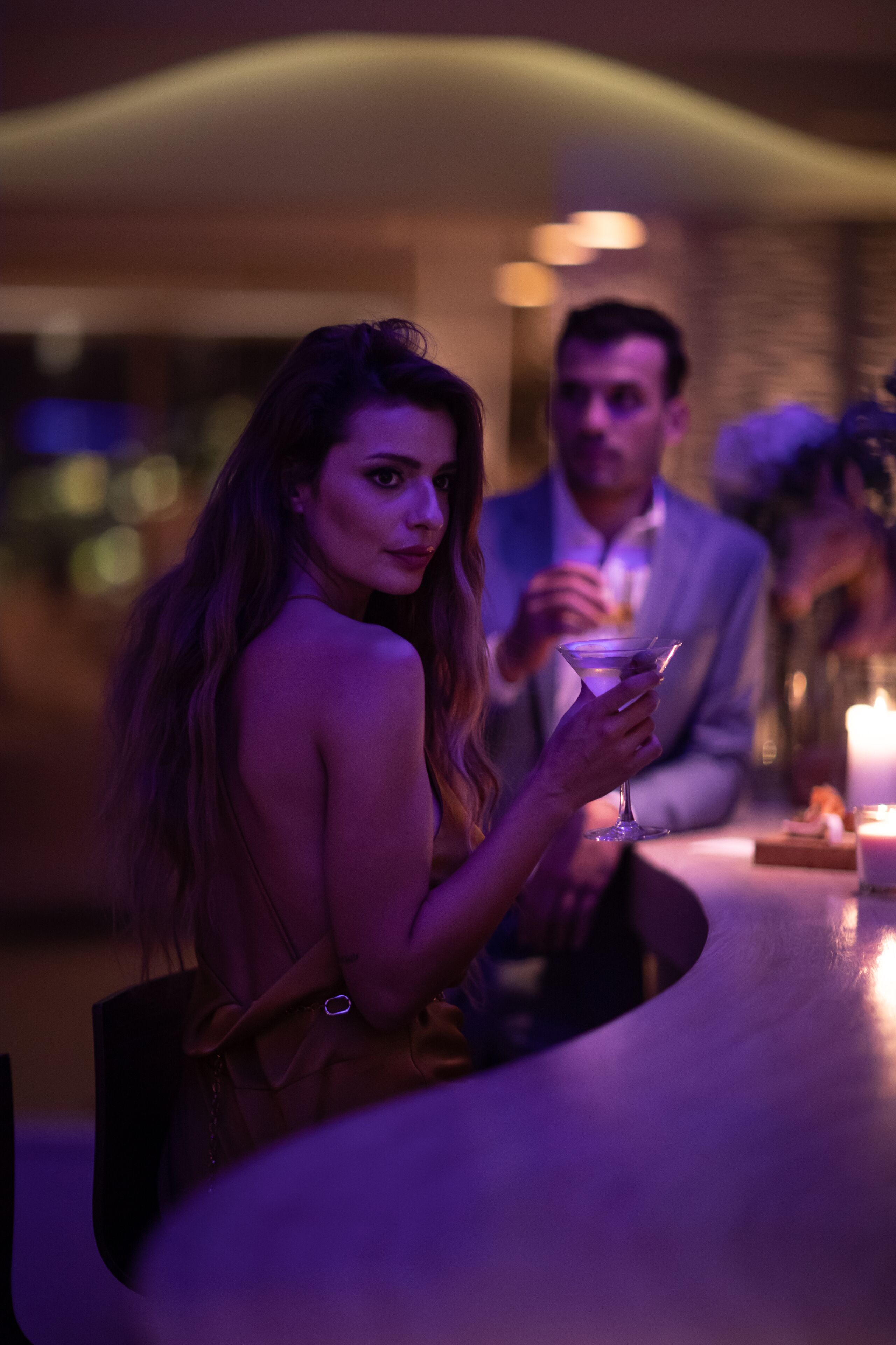 A woman holding a drink at a dimly lit bar with a candle on the table.