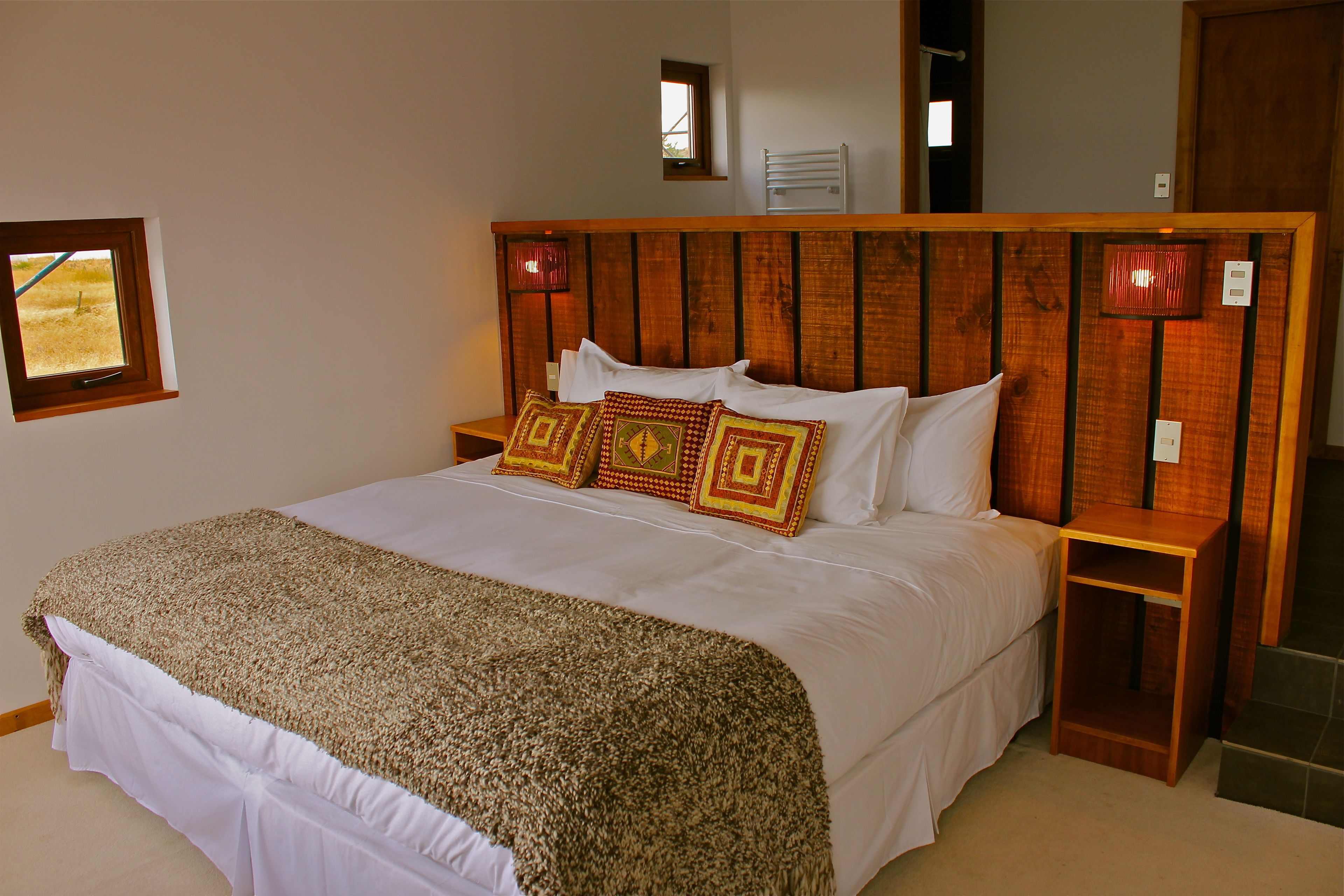 Een slaapkamer met een houten hoofdeinde, een bed met witte lakens en decoratieve kussens.