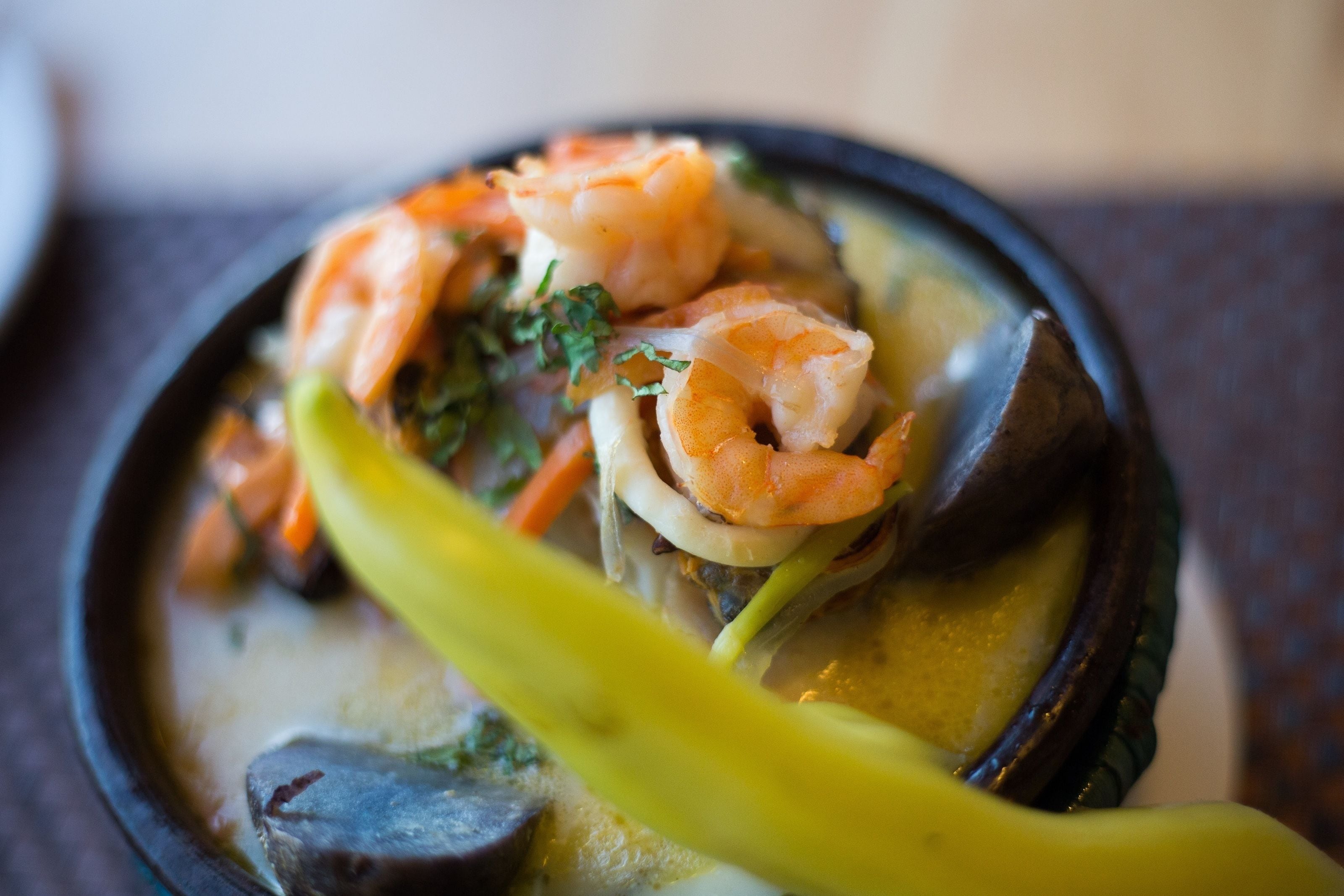 Un tazón de sopa de mariscos con camarones, champiñones y un chile amarillo.