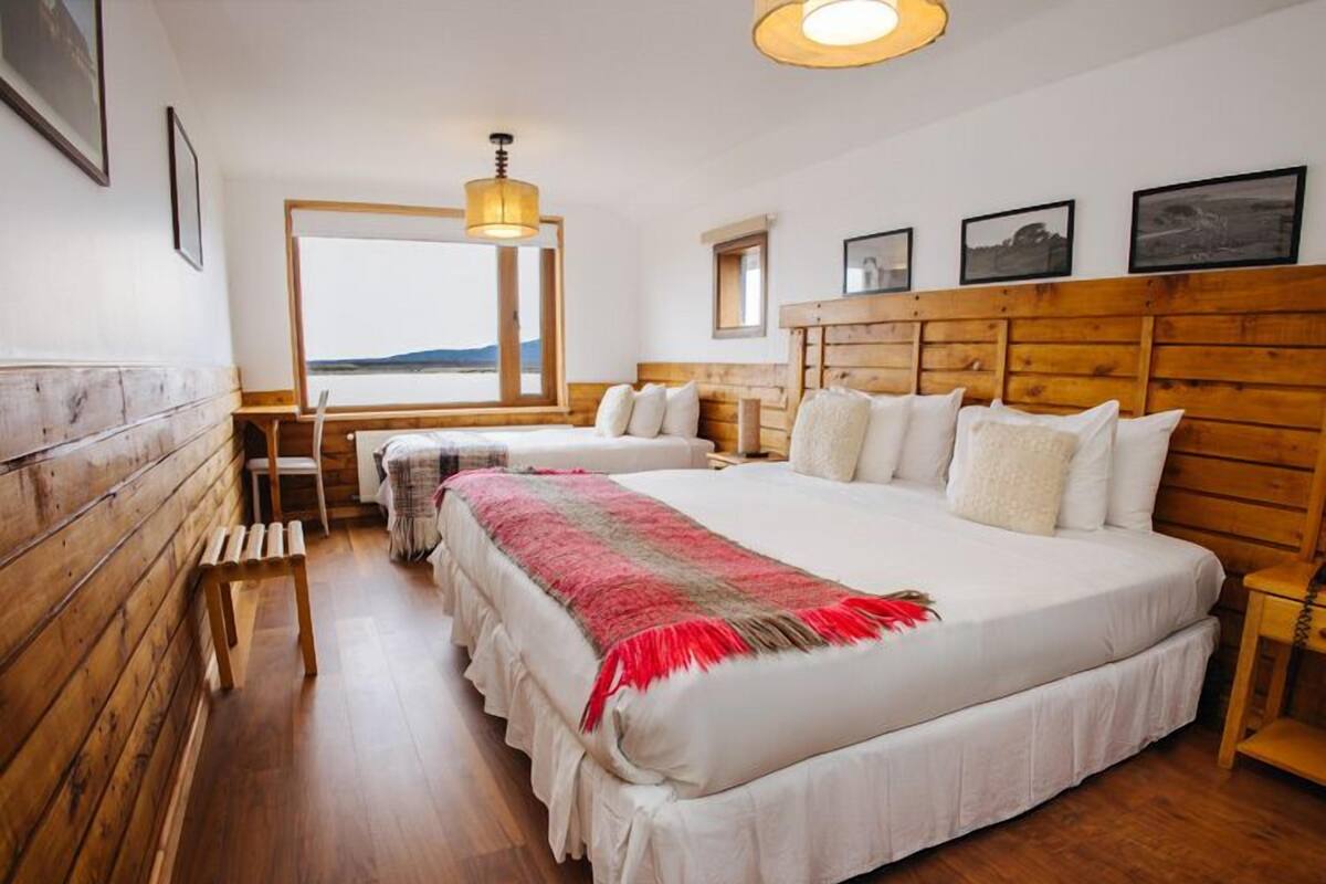 A hotel room with a large bed, a smaller bed, wooden walls, a view of the sea, and a wooden headboard.