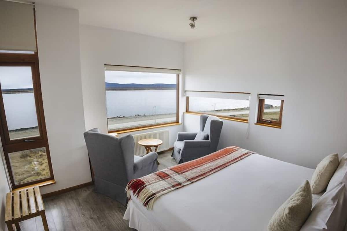A bedroom with a large bed, two chairs, a small table, and a view of the water.