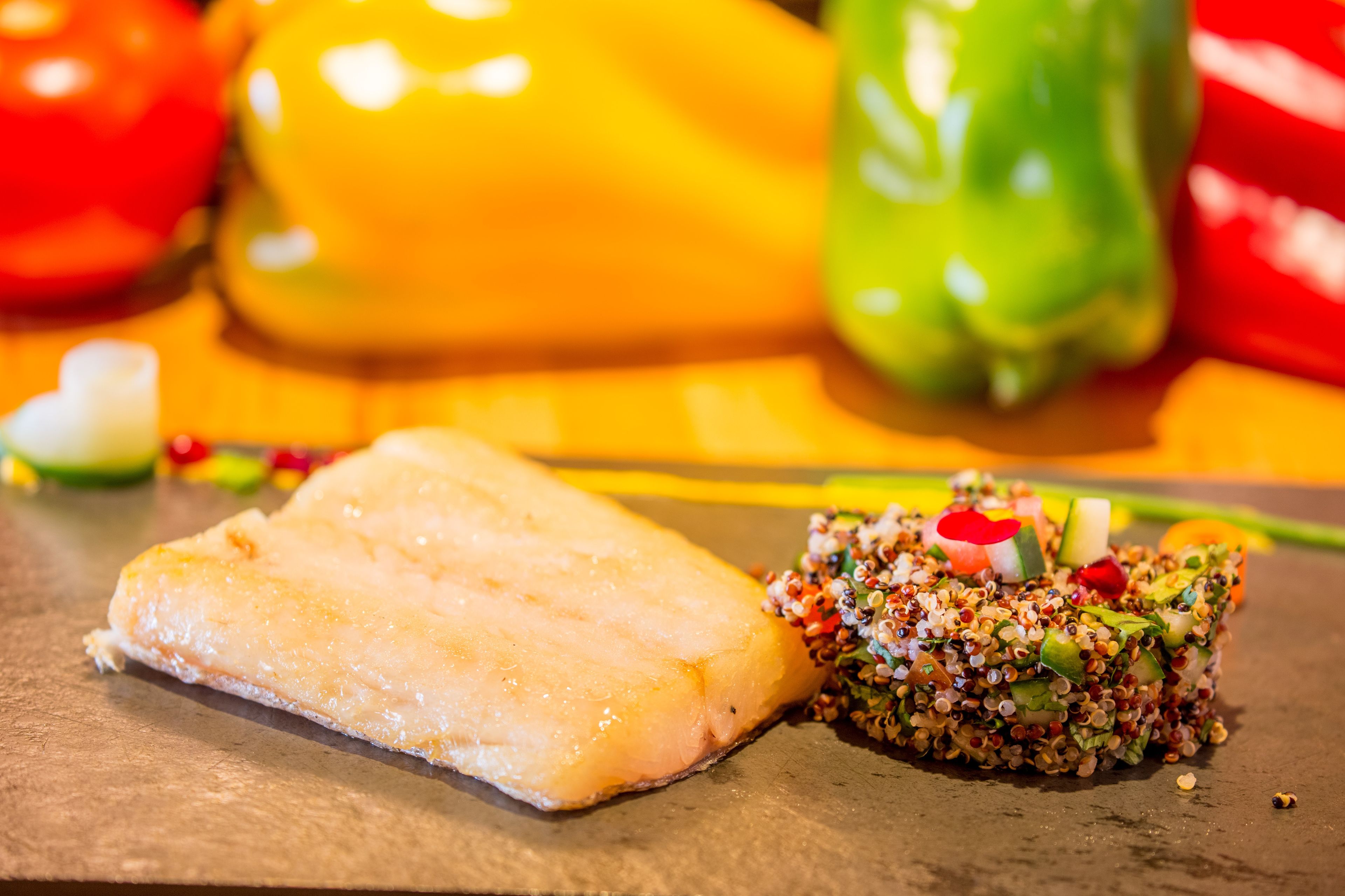 A piece of fish and a quinoa salad with vegetables on a slate surface.
