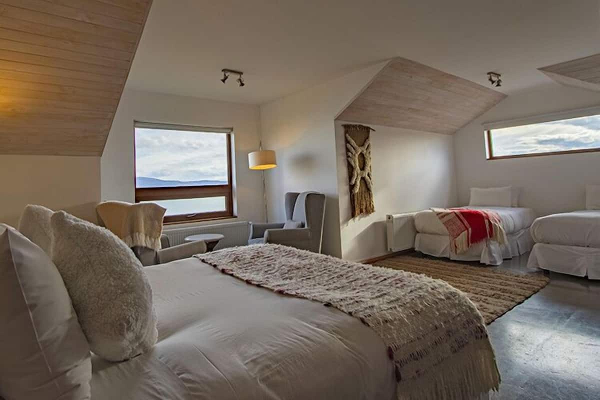 A bedroom with a large bed, a smaller bed, a chair, a desk, and a window with a view.