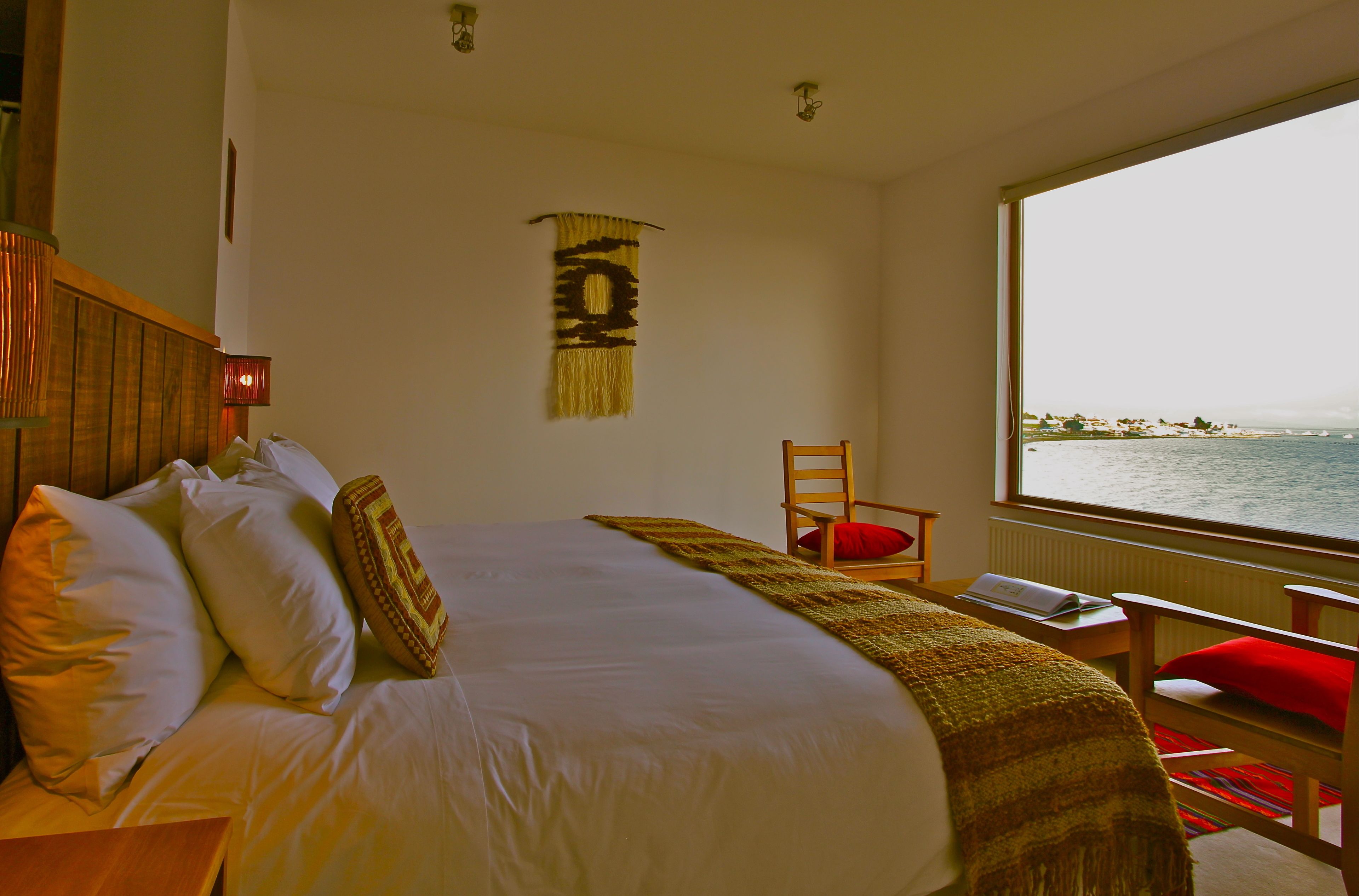 Une chambre avec un grand lit, une chaise, une fenêtre donnant sur la mer et une décoration murale.