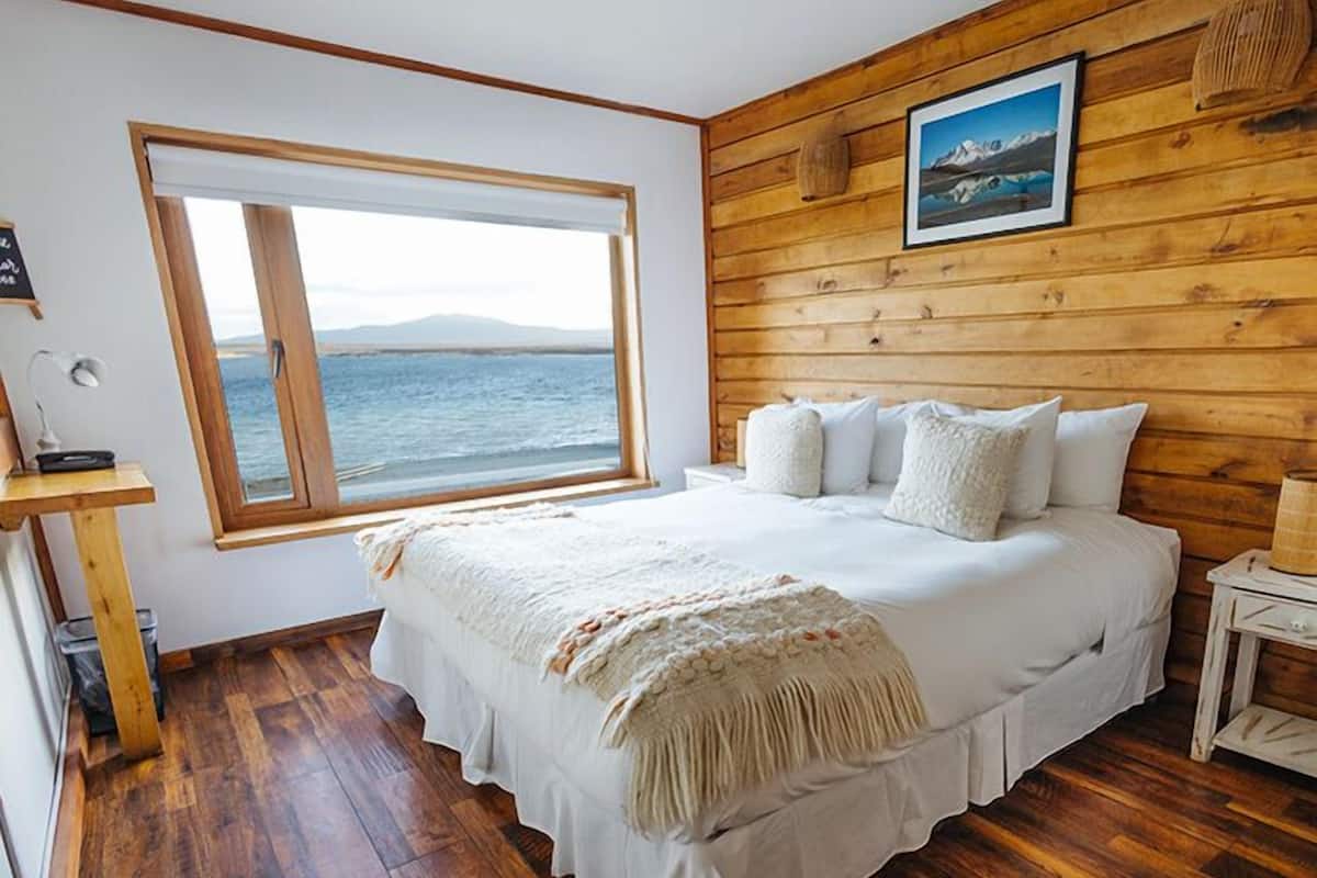 A bedroom with a large window, wooden walls, a bed with white bedding, and a framed picture on the wall.