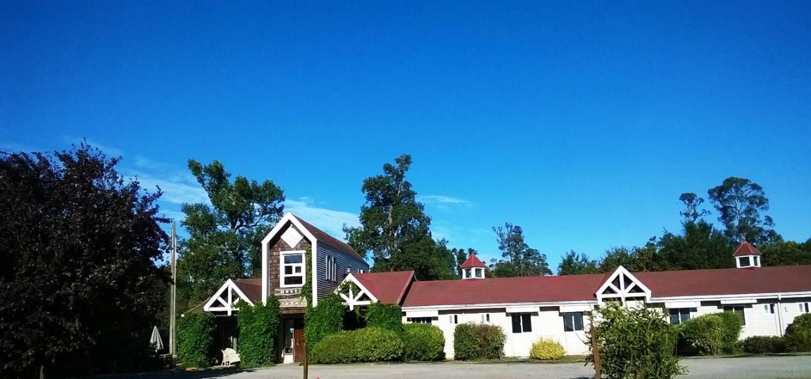 Un hotel con un edificio central y dos estructuras más pequeñas, rodeado de vegetación.