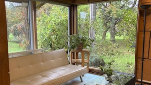 Ein modernes Wohnzimmer mit einem beigefarbenen Sofa, einem Glastisch und Blick auf einen üppigen Garten durch große Fenster.