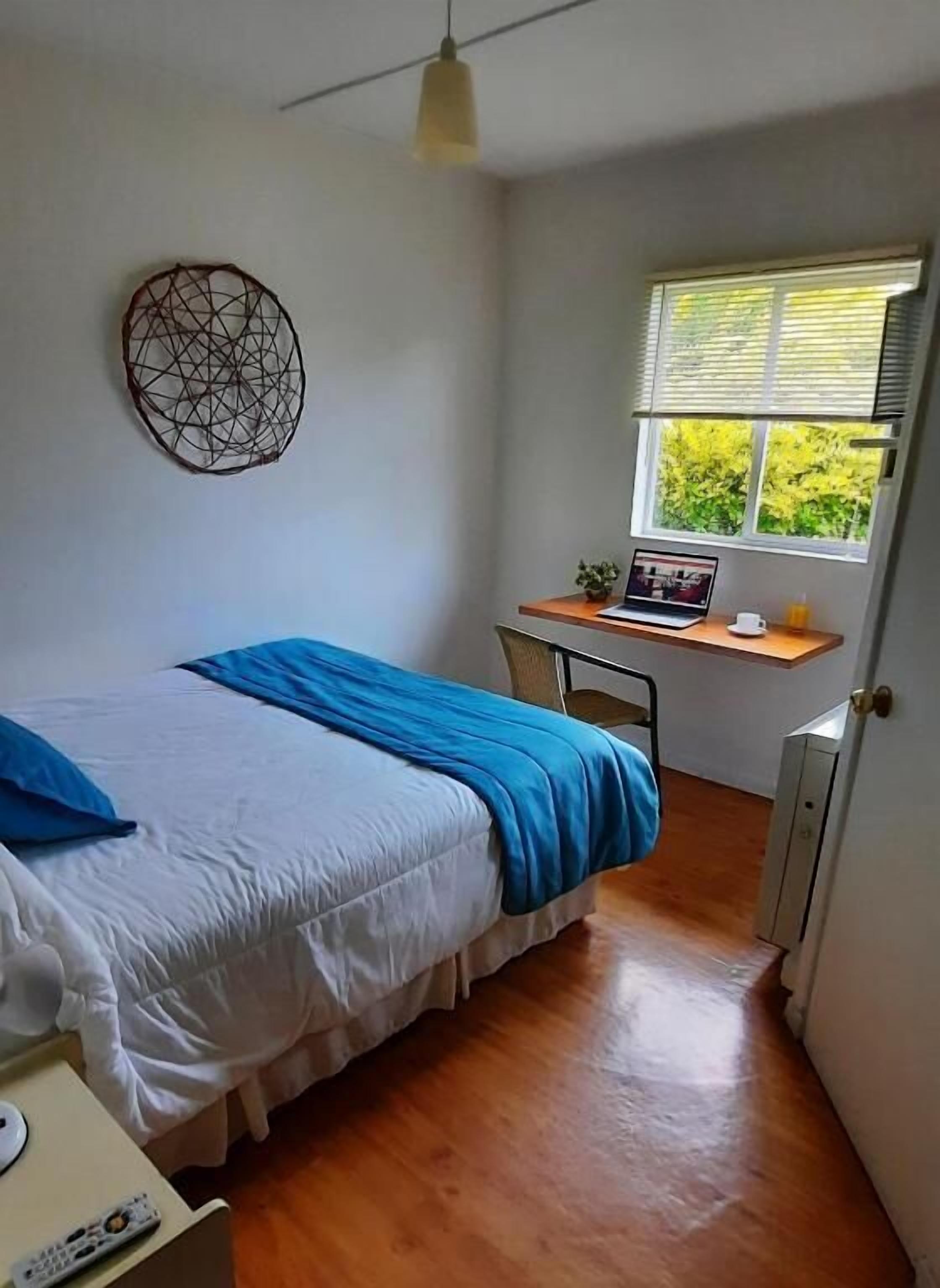 Un dormitorio con cama, escritorio, silla, ventana y un adorno en la pared.