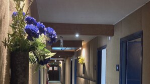 Ein Hotelkorridor mit einer zentralen Blumenkomposition, Türen rechts und einer Decke mit Wolkenmuster.