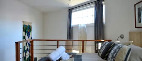 Un letto rifatto con una coperta a motivi, una testiera in legno e una finestra con tende.