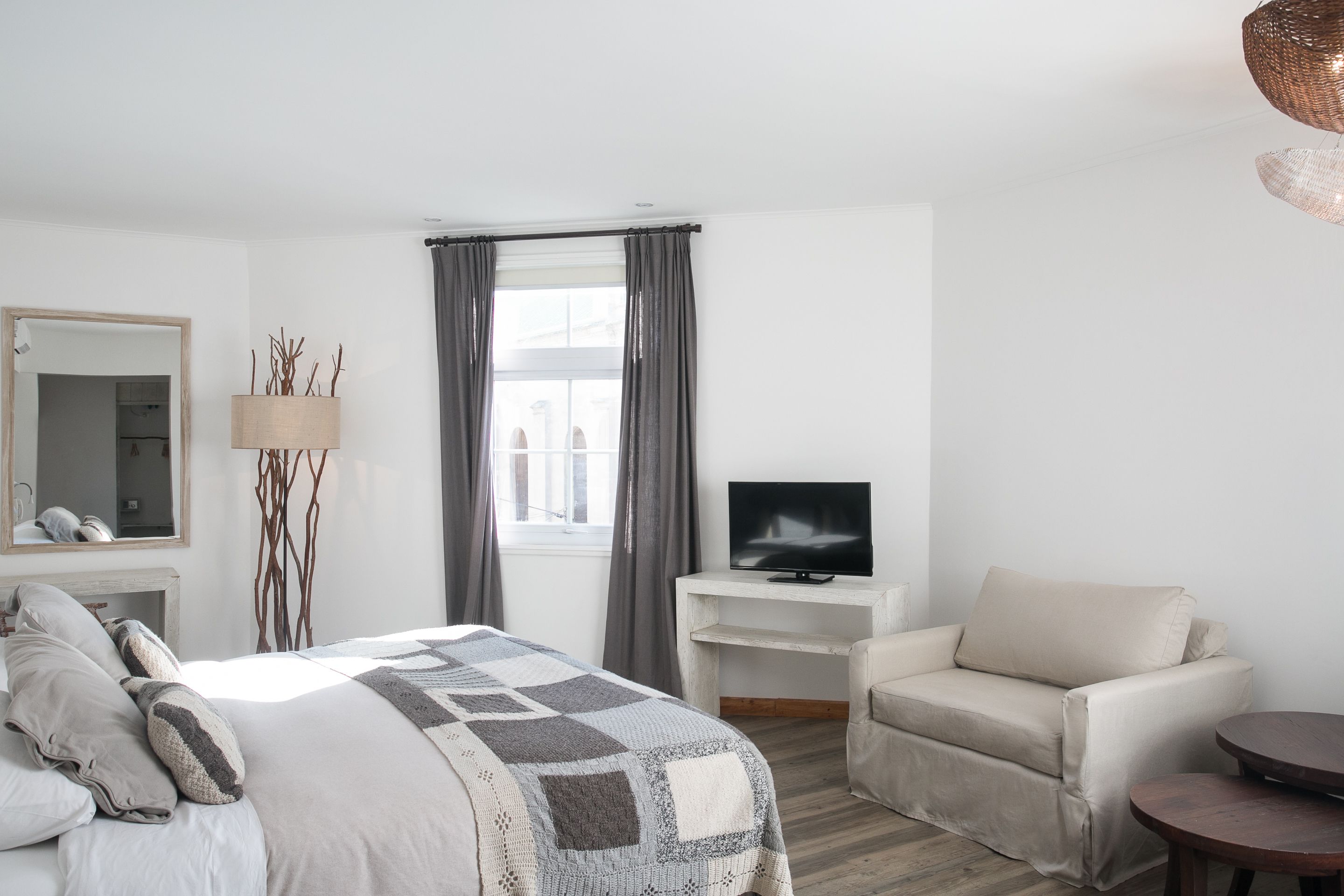 Una habitación de hotel moderna con una cama grande, un televisor en un pedestal, un sofá y una mesita.