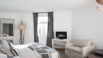Una habitación de hotel moderna con una cama grande, un televisor en un pedestal, un sofá y una mesita.