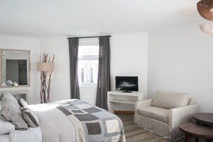 Una habitación de hotel moderna con una cama grande, un televisor en un pedestal, un sofá y una mesita.