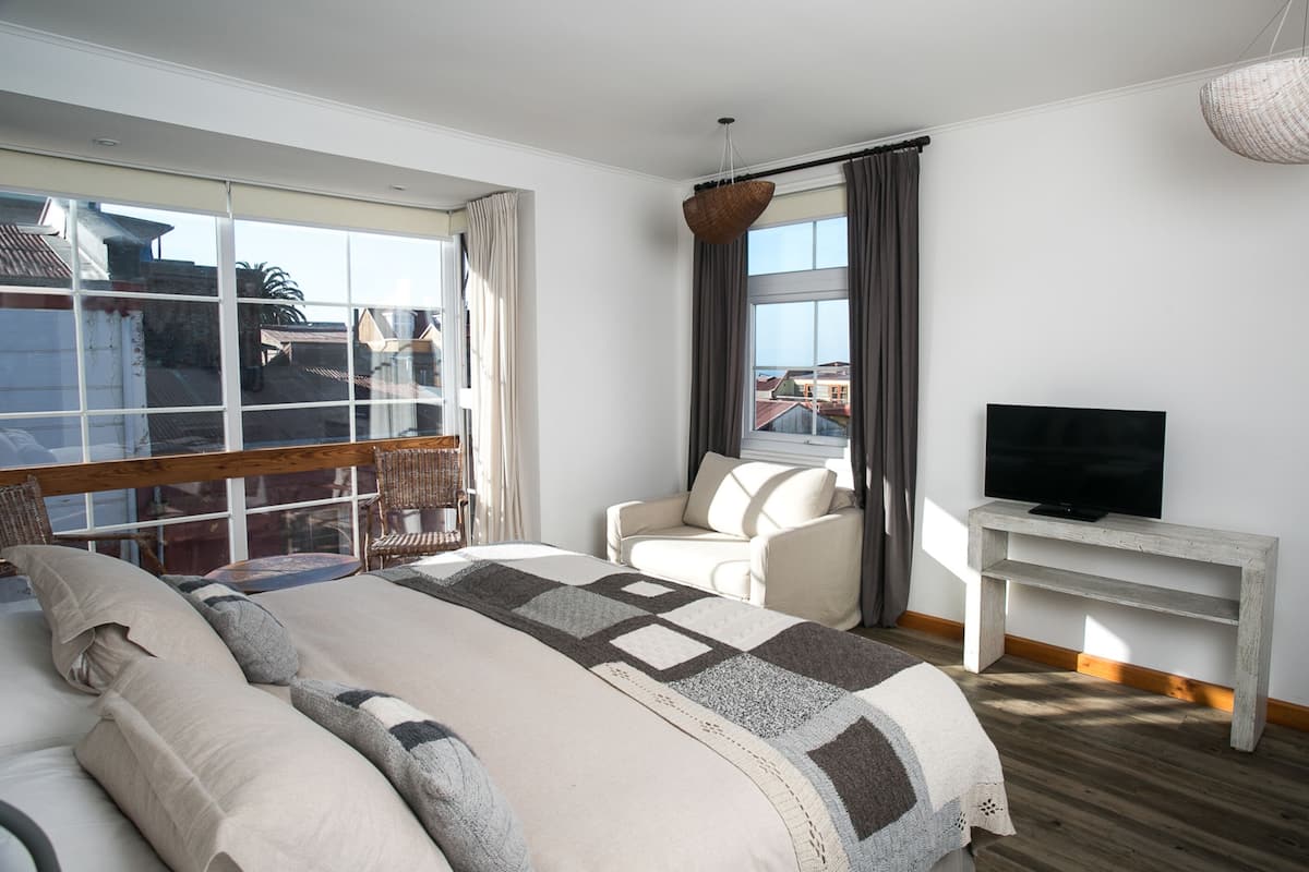Une chambre d’hôtel avec un grand lit, un canapé, un téléviseur posé sur un meuble en bois et un balcon donnant sur des immeubles.