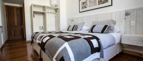 A bedroom with a wooden floor, a bed with a patterned blanket, a white headboard, and a framed picture on the wall.