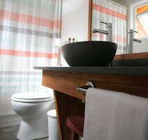 Un baño con un lavamanos negro, inodoro blanco y cortinas a rayas.