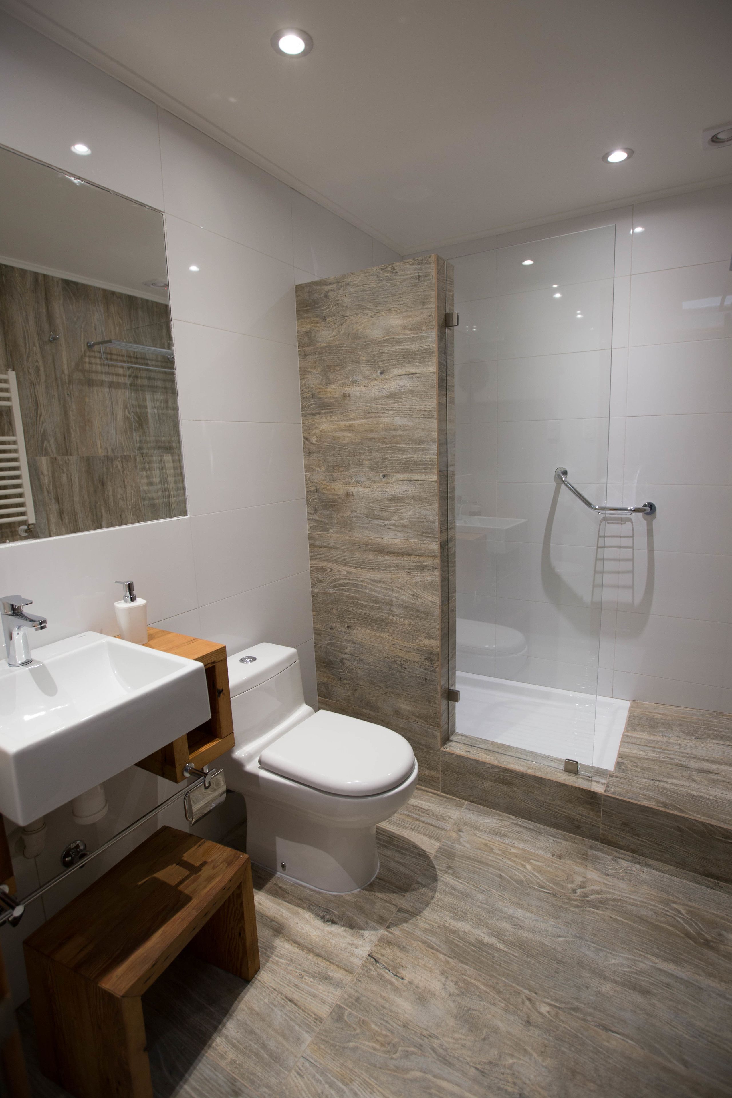 Une salle de bain moderne avec un lavabo blanc, un meuble-lavabo en bois, des toilettes et une douche séparée par une paroi de verre.