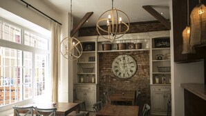 A dining area with wooden tables and chairs, a large wall clock, and shelves with kitchen utensils. - Casa Galos Hotel & Lofts (Valparaiso)