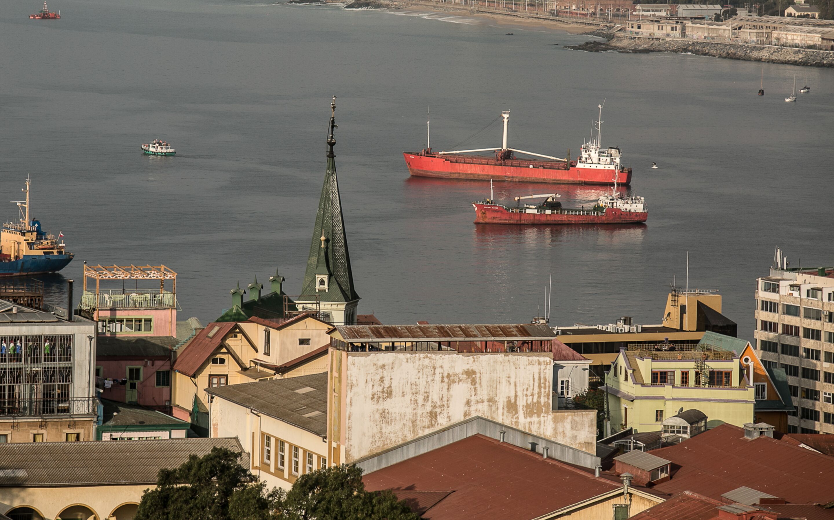 Un puerto con un gran barco rojo, edificios de arquitectura diversa y una aguja de iglesia.