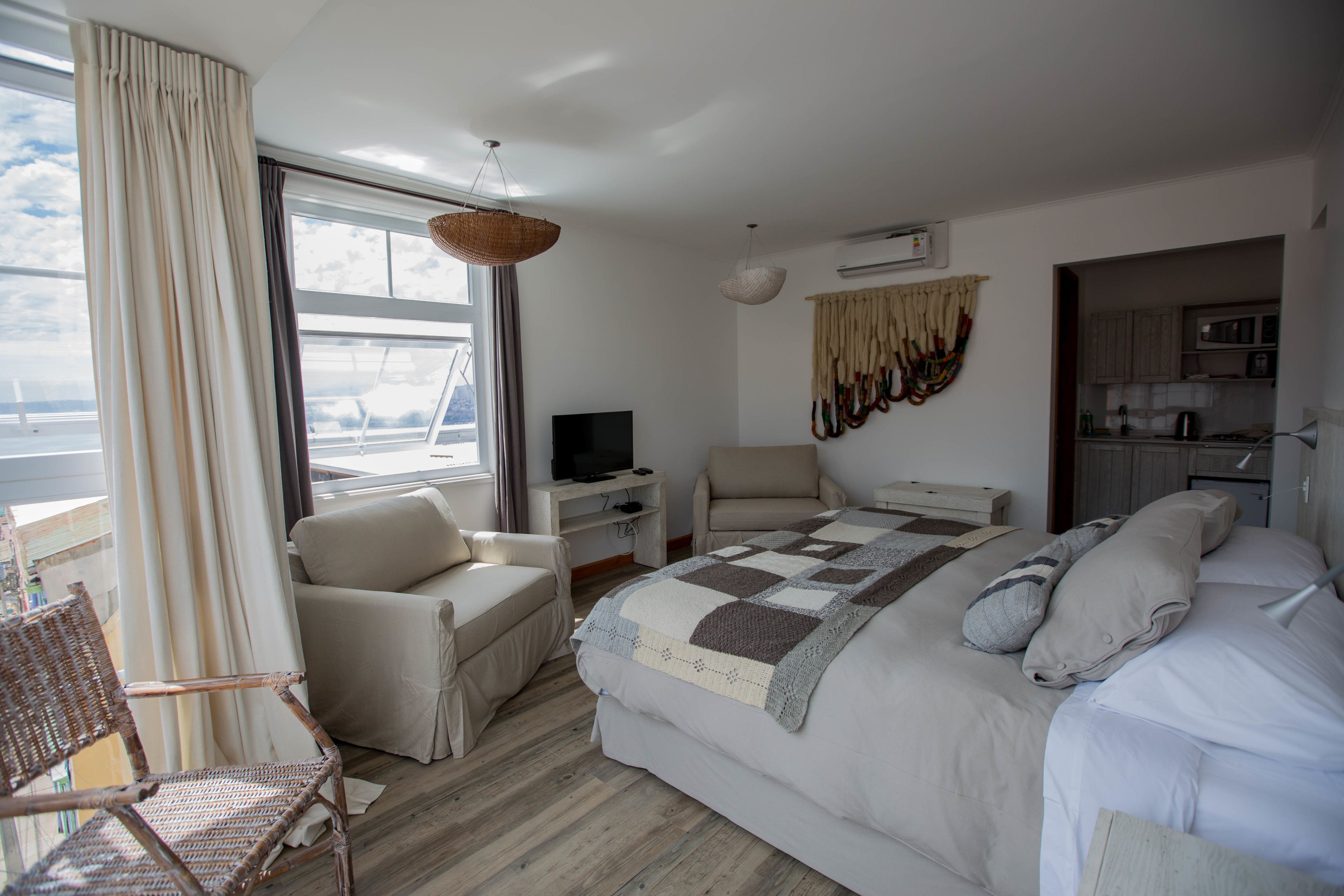 Quarto de hotel com cama, poltrona, escrivaninha, televisão e vista para o exterior.
