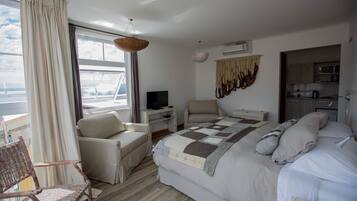 Quarto de hotel com cama, poltrona, escrivaninha, televisão e vista para o exterior.