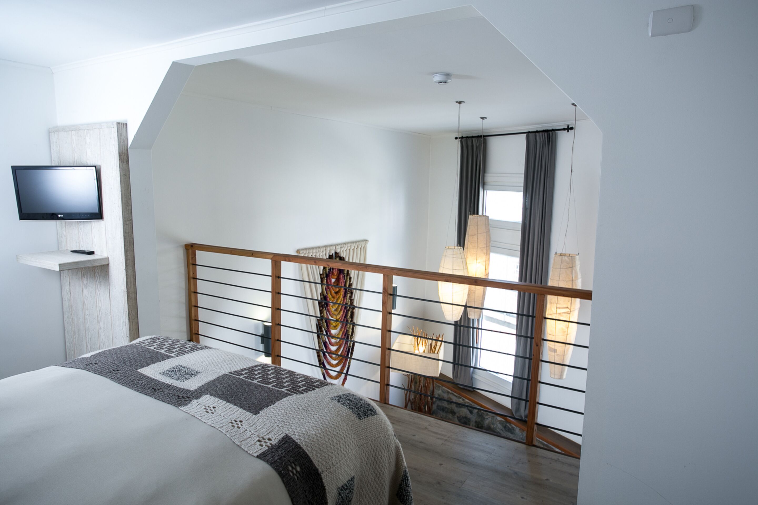 Une chambre à coucher comprenant un lit, une télévision, une fenêtre avec des rideaux et un escalier menant à un étage supérieur.