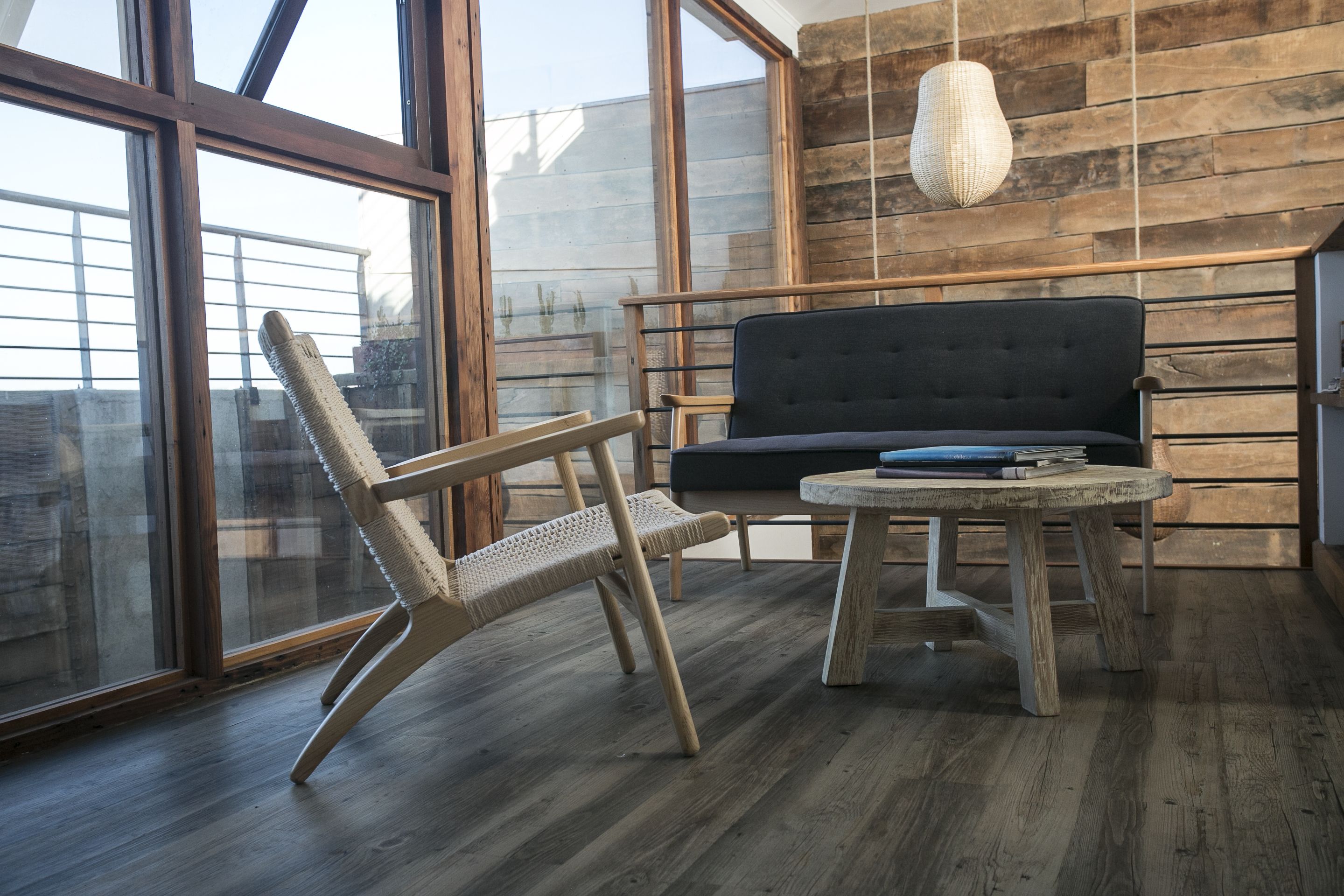 Un interior moderno con piso de madera, un sofá oscuro, un sillón de mimbre y una mesa redonda.