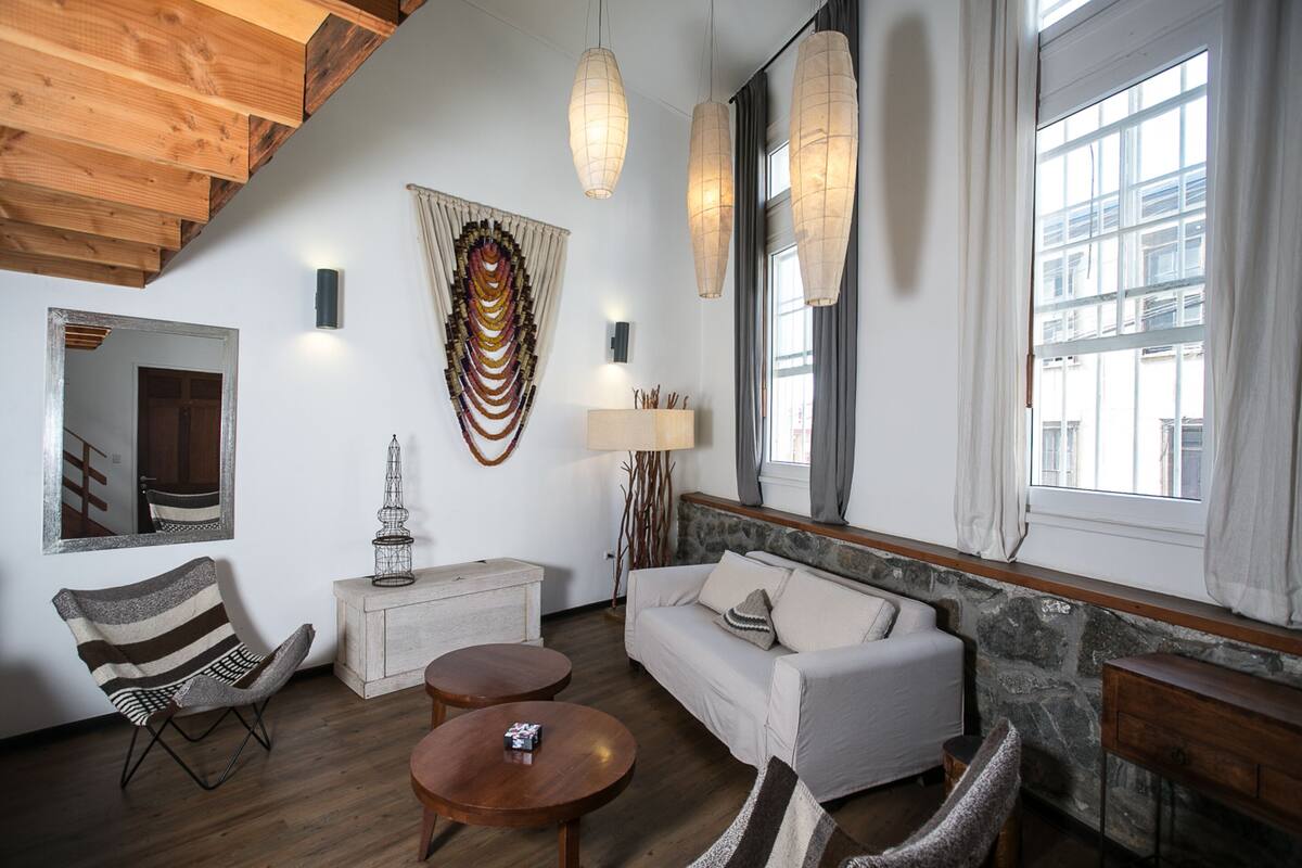 Un salon moderne avec un plafond en bois, un canapé blanc, une table basse en bois, un fauteuil à rayures et un mur d’accent en pierre.