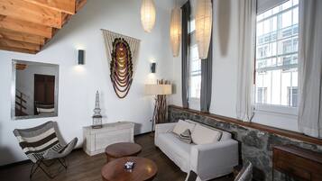 A modern living room with a wooden ceiling, a white sofa, a wooden coffee table, a striped armchair, and a stone accent wall.