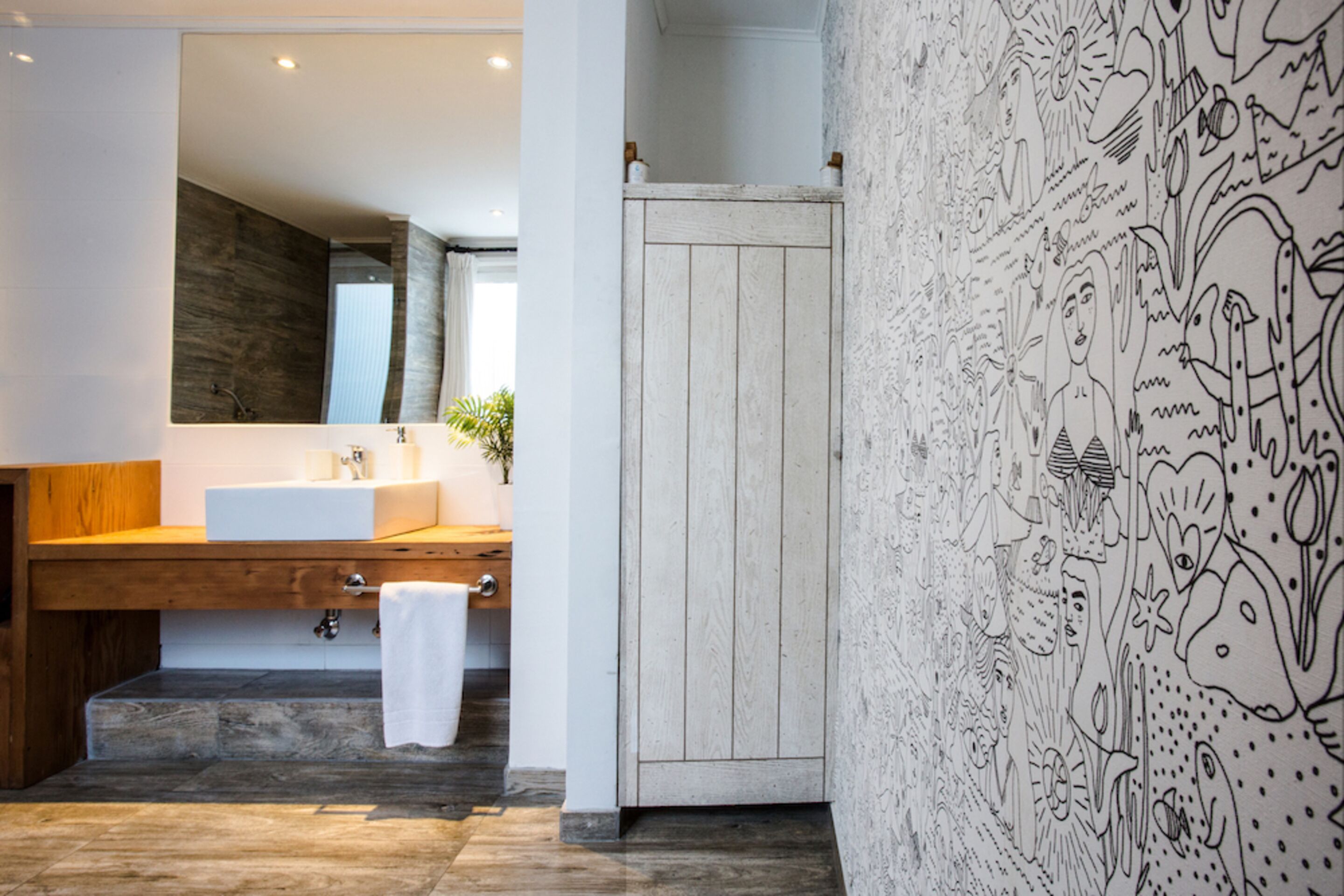 Un baño moderno con un espejo grande, tocador de madera y una puerta blanca.