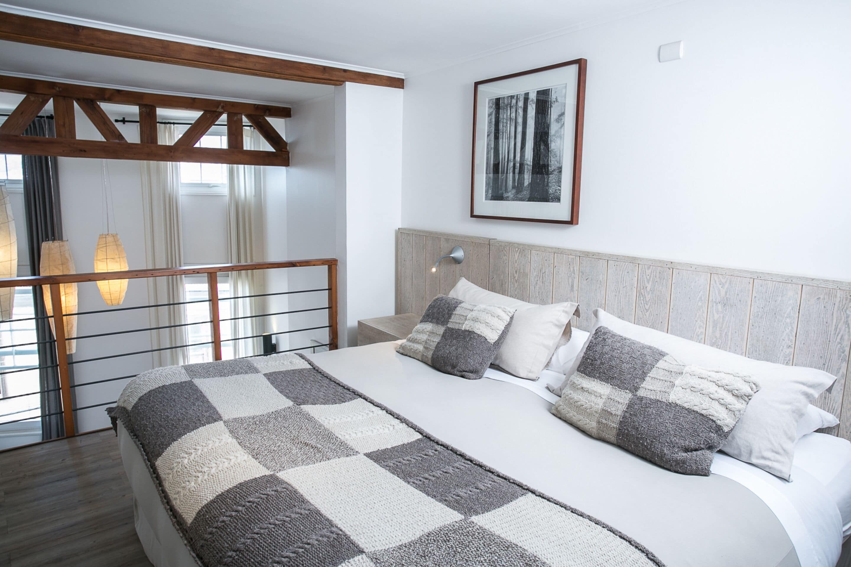 Un dormitorio con una cama grande, cabecera de madera, manta a cuadros y un cuadro en la pared.