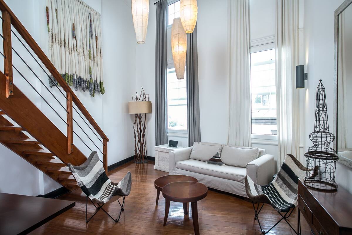 Un salon moderne avec un escalier en bois, un canapé blanc, des fauteuils à rayures et une table basse.