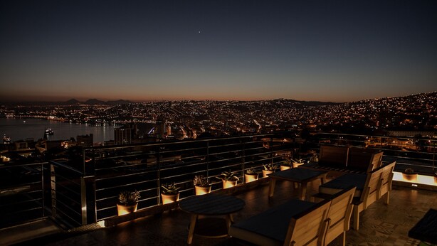 A rooftop terrace with seating and potted plants, overlooking a cityscape at dusk. - Casa Galos Hotel & Lofts (Valparaiso)