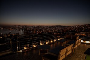 A rooftop terrace with seating and potted plants, overlooking a cityscape at dusk. - Casa Galos Hotel & Lofts (Valparaiso)