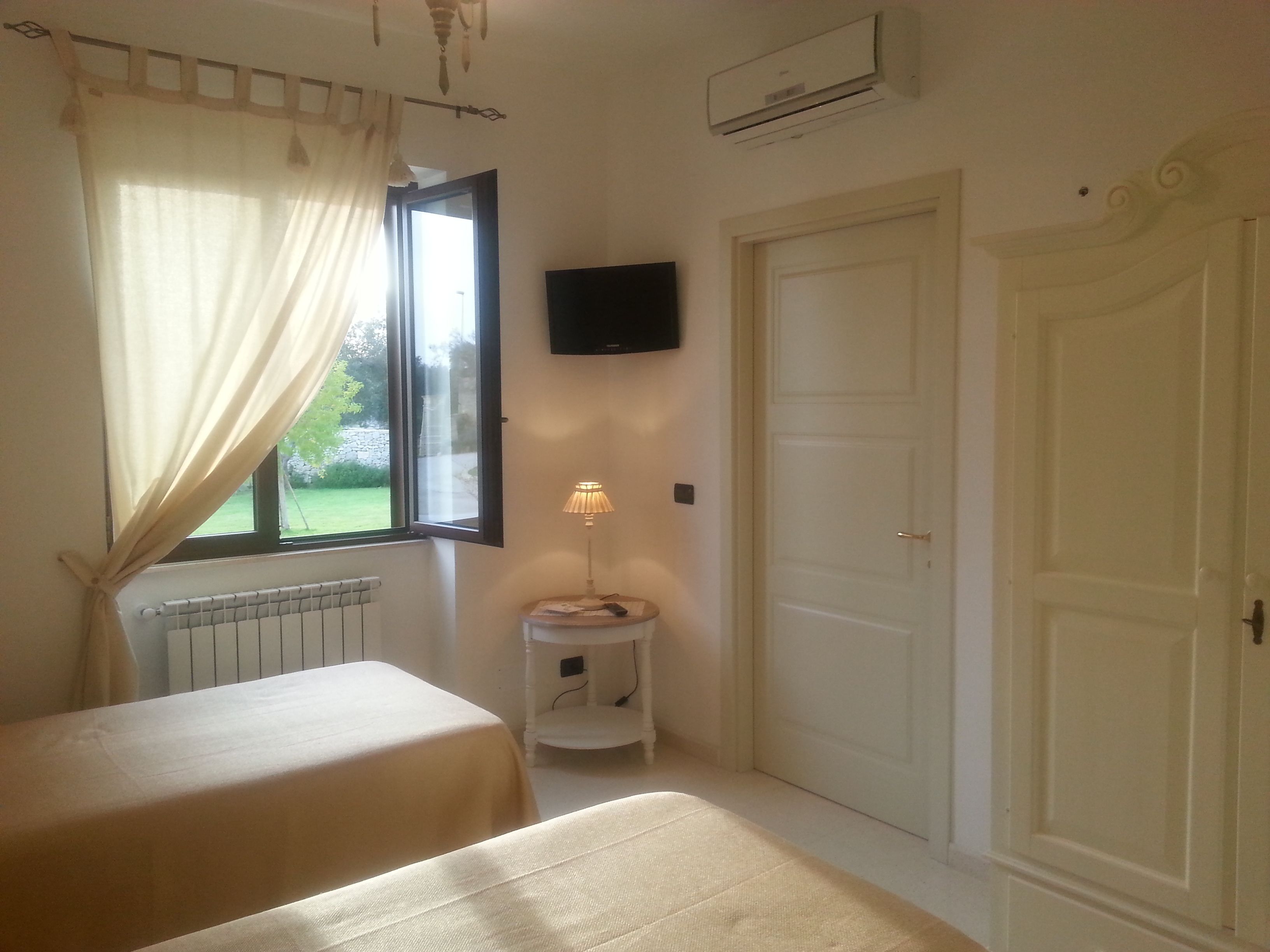 A bedroom with two beds, a window with curtains, a bedside lamp, a TV mounted on the wall, and a door.